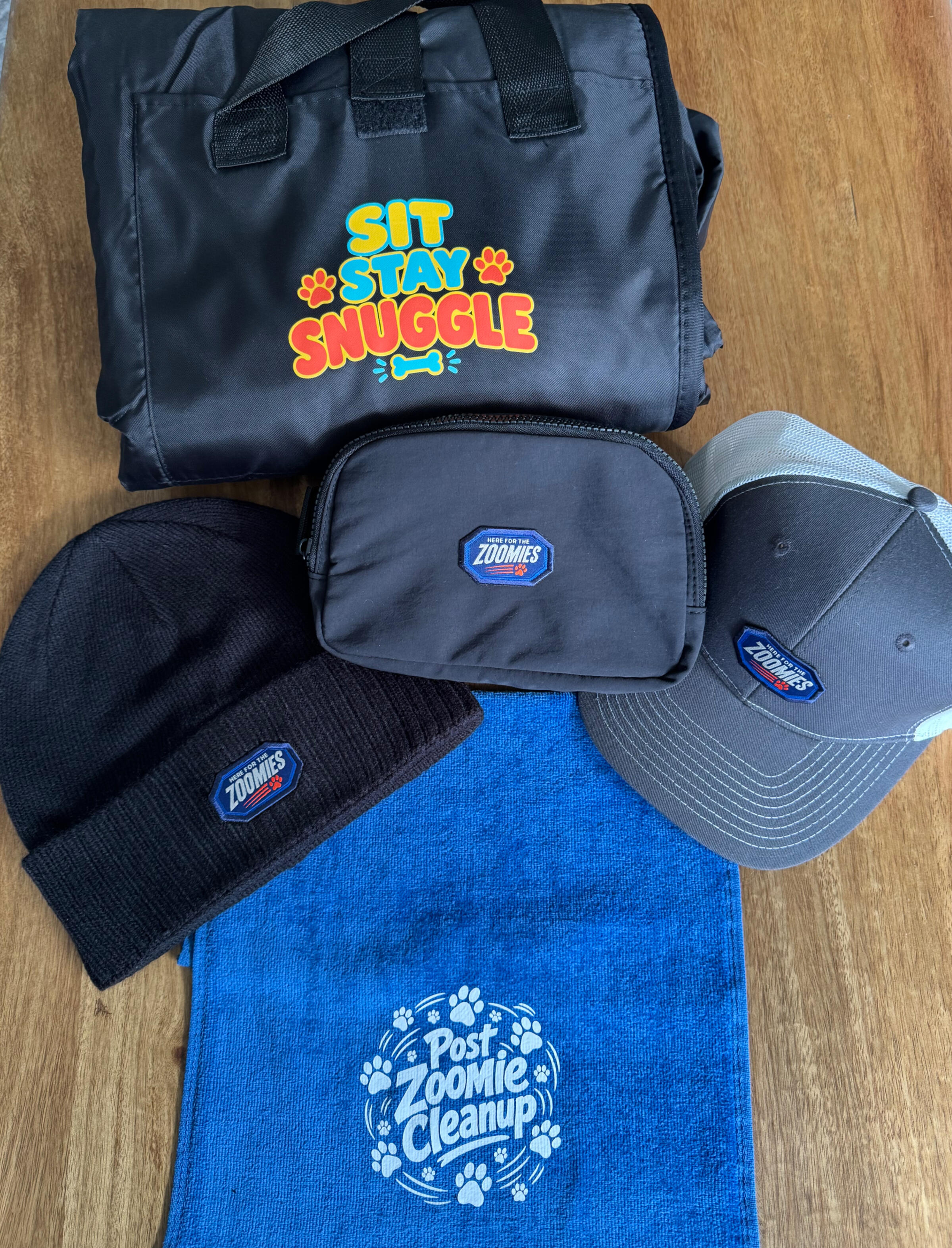 Custom dog rescue event collection with decorated bag, pouch, hats, and blue towel on a wooden table.